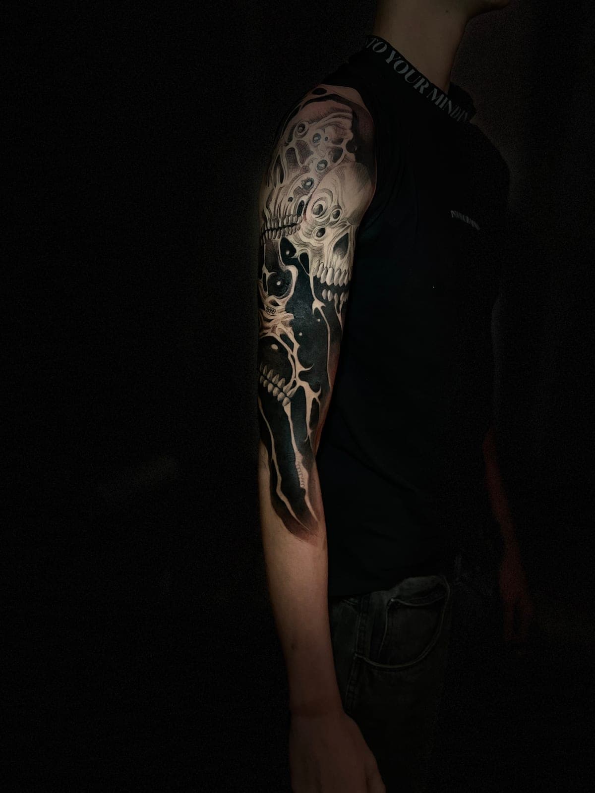 Manga completa de brazo con un cráneo y fondo en negro sólido, fotografiada con luz lateral